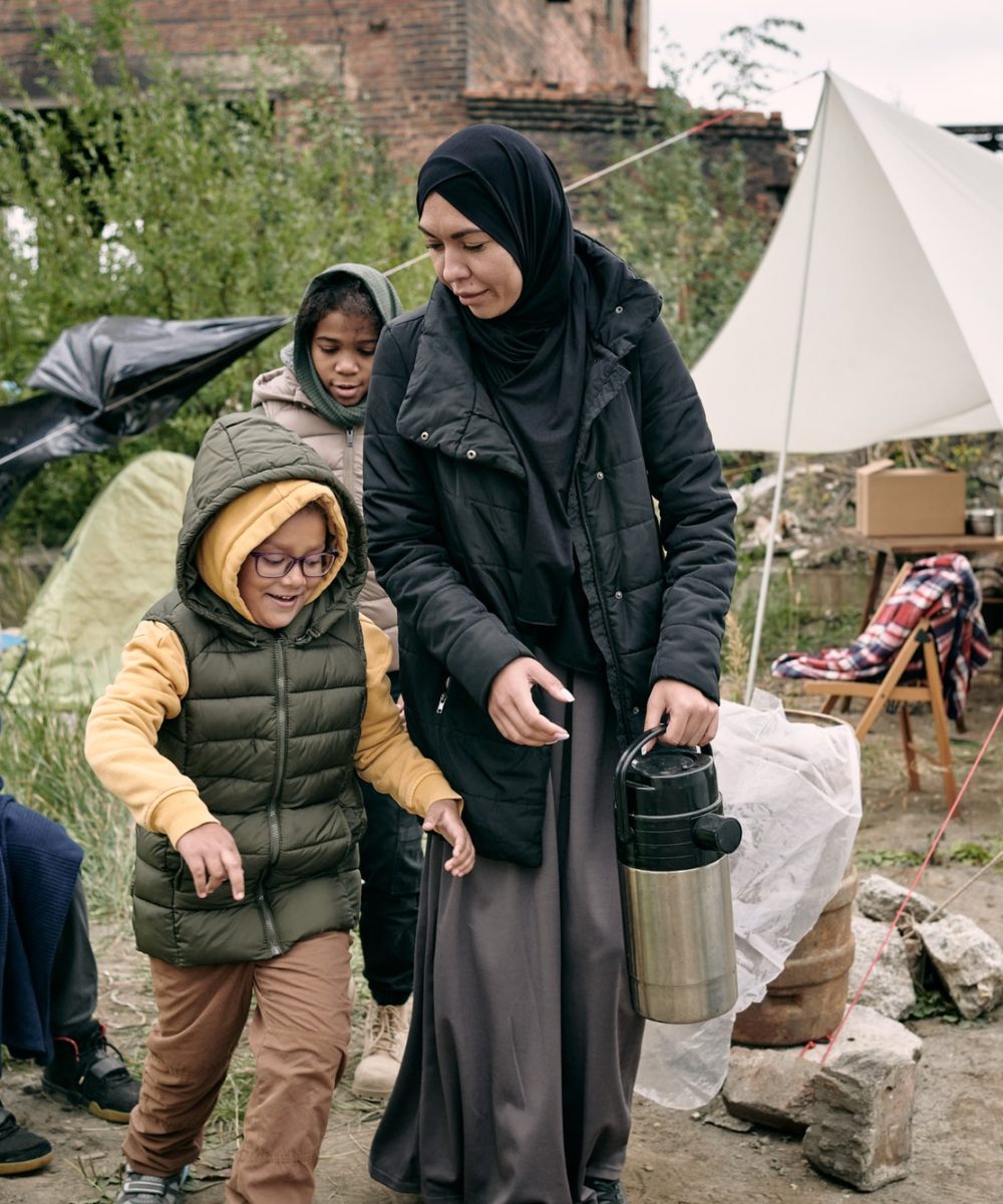 mother-carrying-thermos-flask-along-refugee-camp.jpg